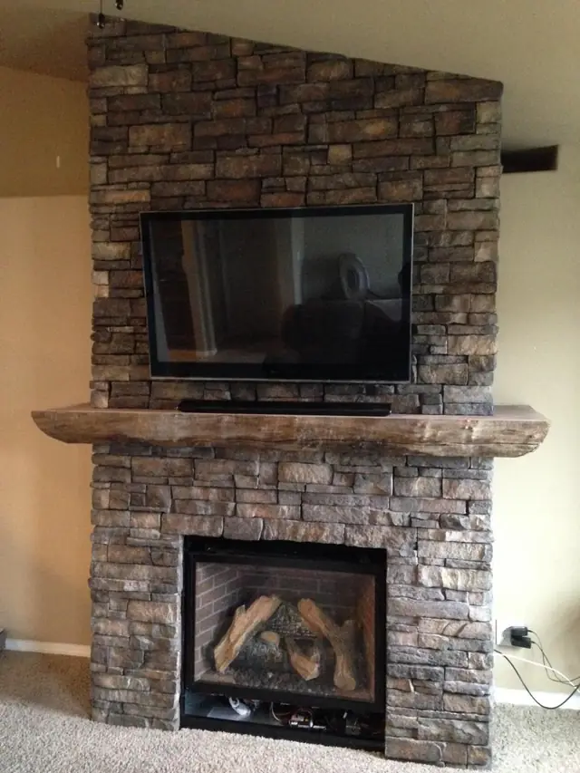 A stone-veneer gas fireplace with a timber mantel