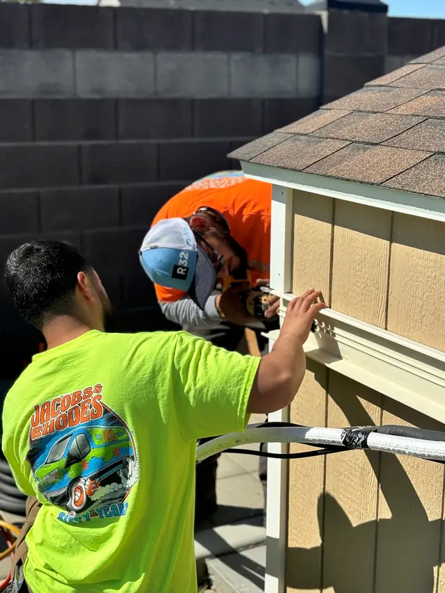 Two Jacobs and Rhodes installers in hi-vis shirts fitting a line-set cover on an outdoor unit